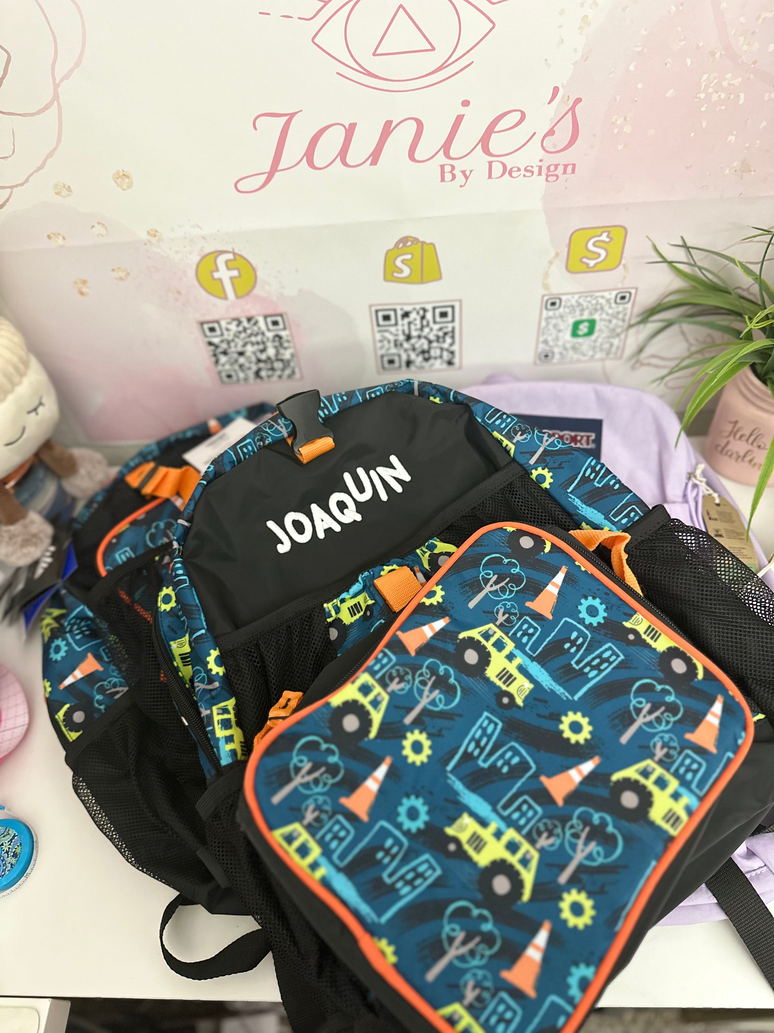 A personalized embroidered backpack with various designs including a car, truck, and construction vehicle, with the name 'Joaquín' embroidered on the front.