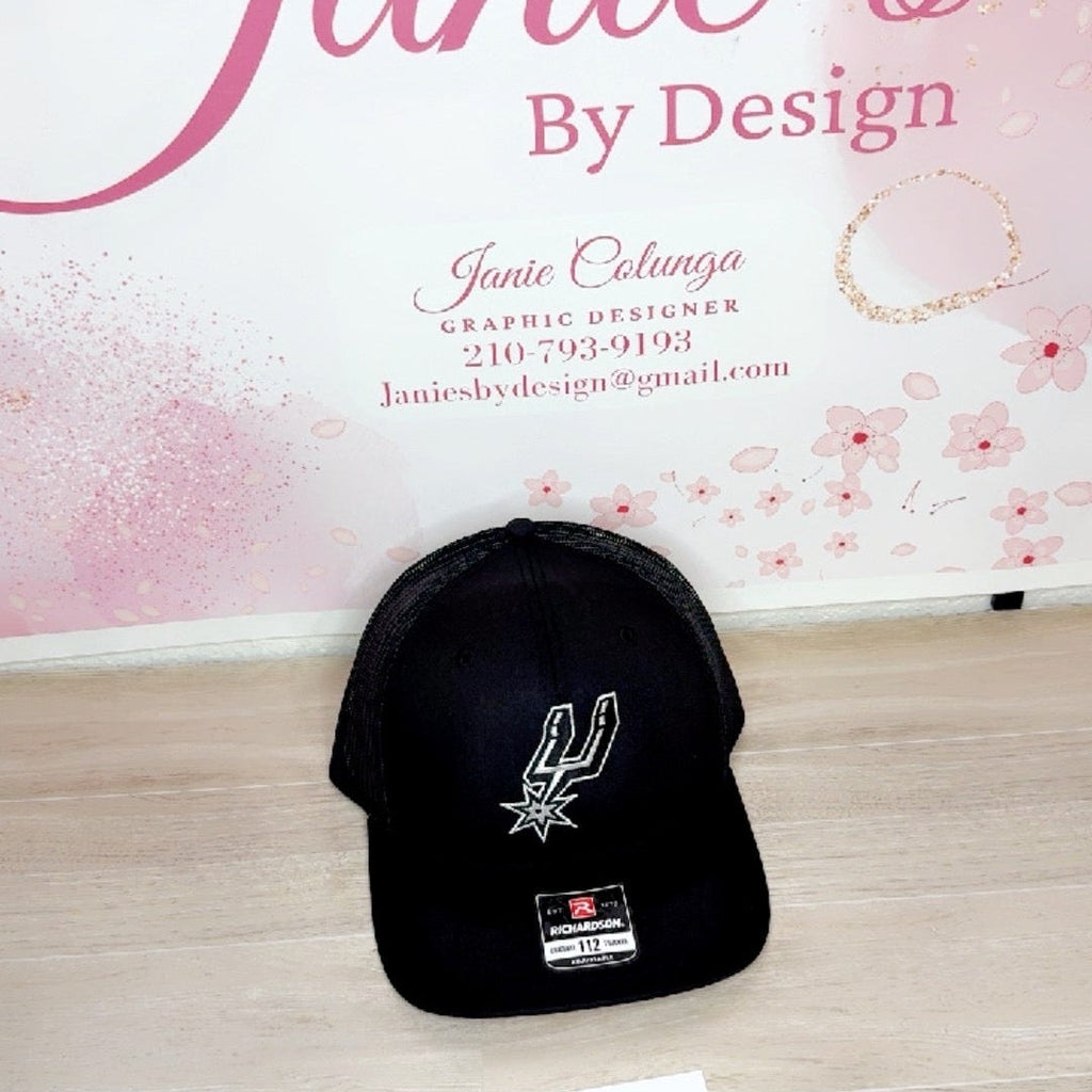 Black cap with a logo on a wooden surface with a pink floral background