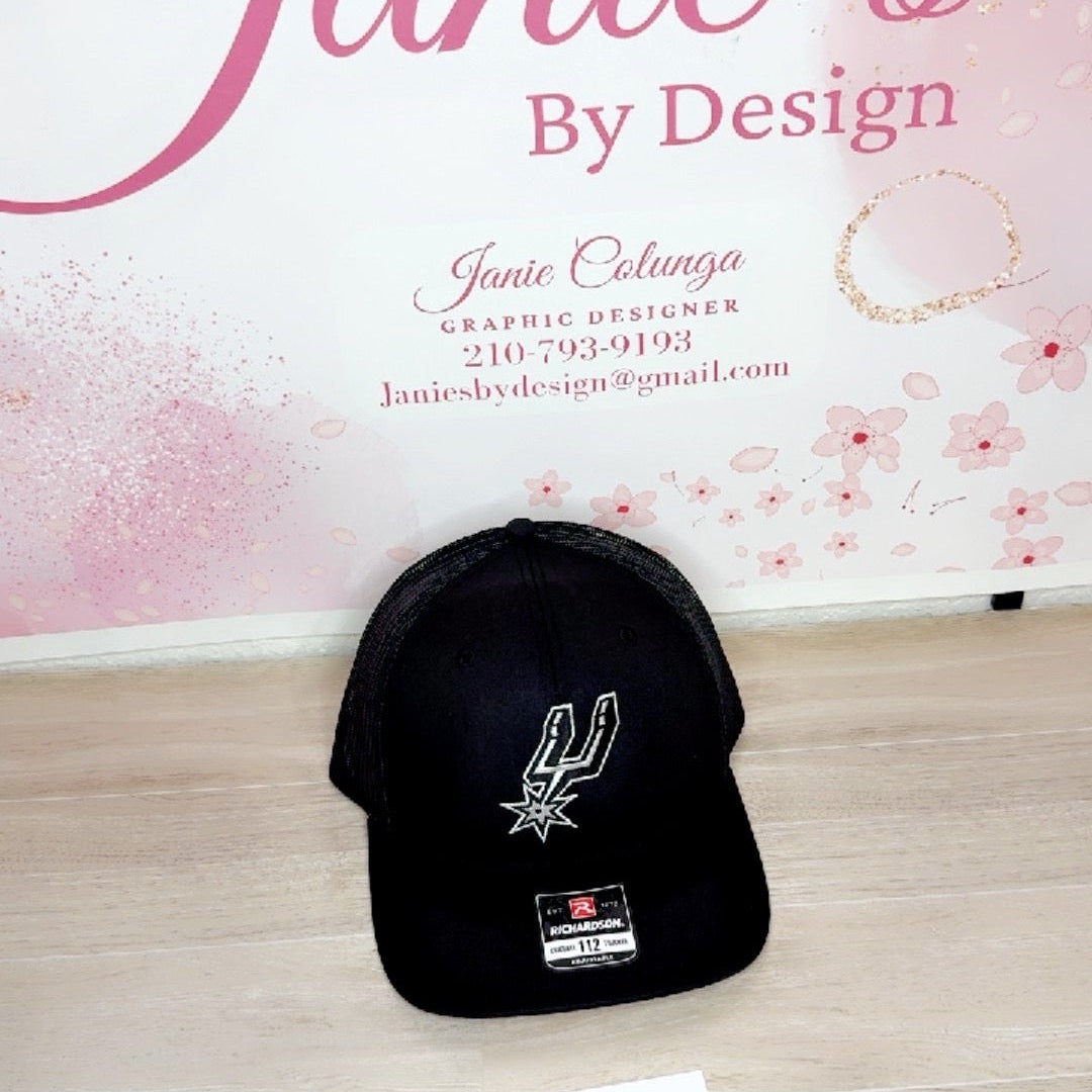 Black cap with a logo on a wooden surface with a pink floral background