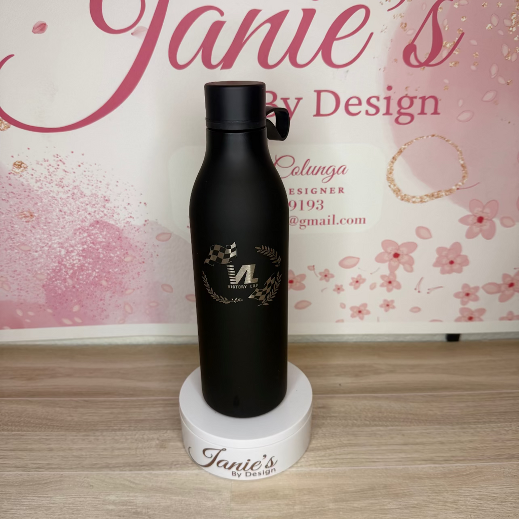 Black water bottle with branding on a wooden surface and floral background