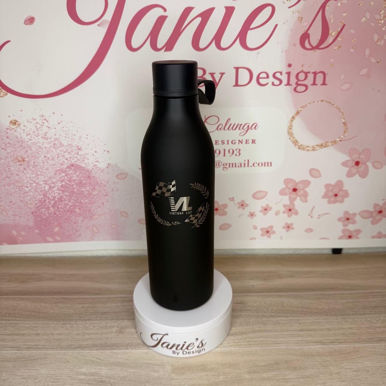 Black water bottle with branding on a wooden surface and floral background