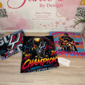 Three custom printed t-shirts displayed on a light wood floor in front of a pink 'Janie's By Design' graphic backdrop. The shirts feature custom designs: a black Spurs 2020 Champions shirt, a blue and red San Antonio Spurs shirt, and a blue and red Lakers shirt with 'WENDBYANYAMA' text.