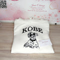 A folded white hoodie with a black graphic print of a dog and the word 'KOBE' is displayed on a light wood surface in front of a pink branded backdrop reading 'Janie's By Design'.