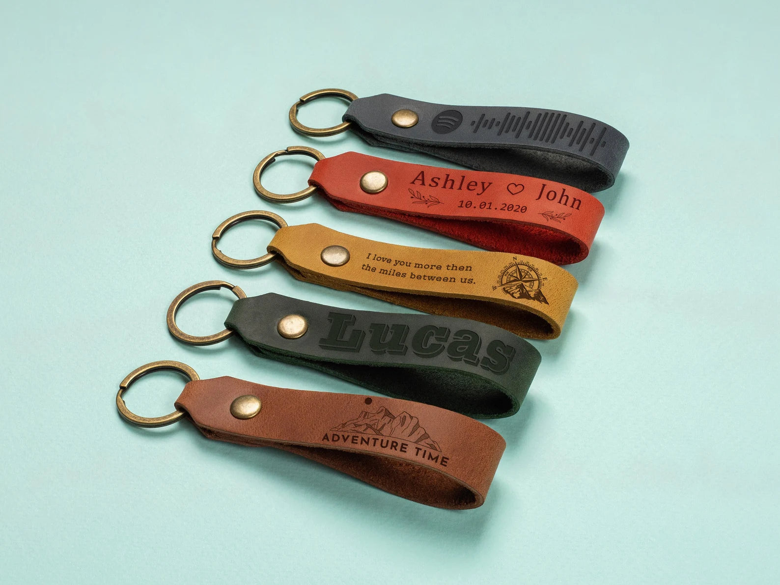 Five leather keychains with engraved text on a light blue background